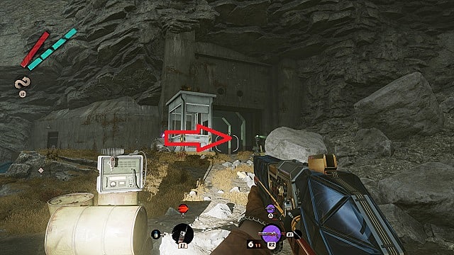 Le personnage du joueur regarde l'entrée du bunker de Fia à l'intérieur d'une falaise, avec une flèche pointant vers la salle des codes.
