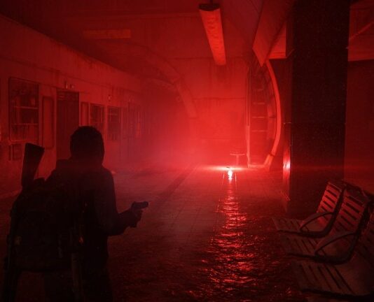 Ellie walking through dark subway lit by a red flare.