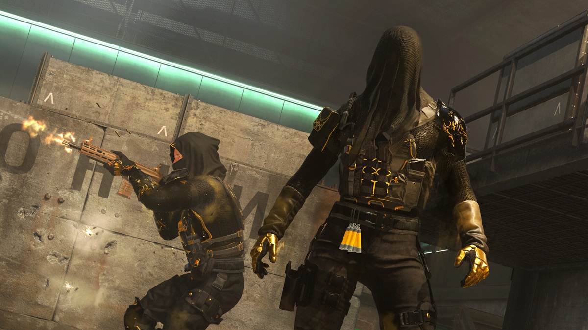 Un opérateur en noir et or avec une cagoule noire se tient devant un autre opérateur qui tire.